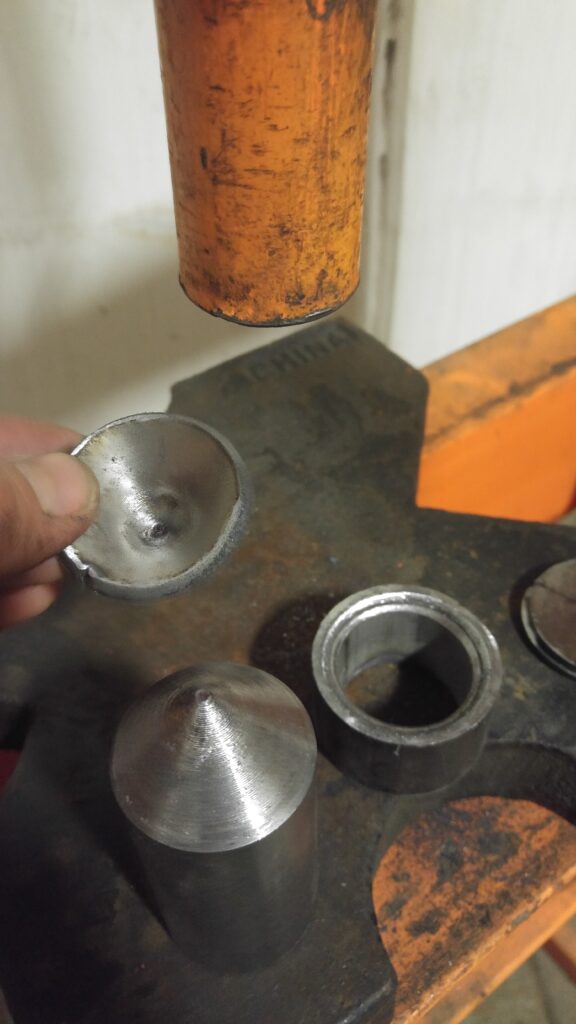 A freshly formed cap held above the die, with the punch alongside