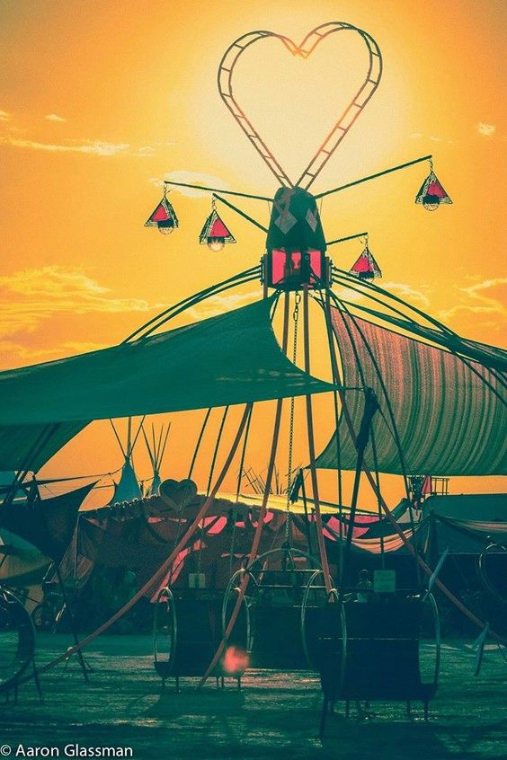 The Dream Swing silhouetted at daybreak, heart-topped mast and lantern arms against an orange sky