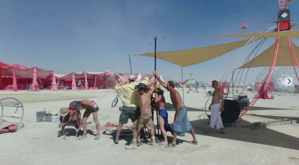 A crew of campmates raising the Dream Swing’s mast on the playa