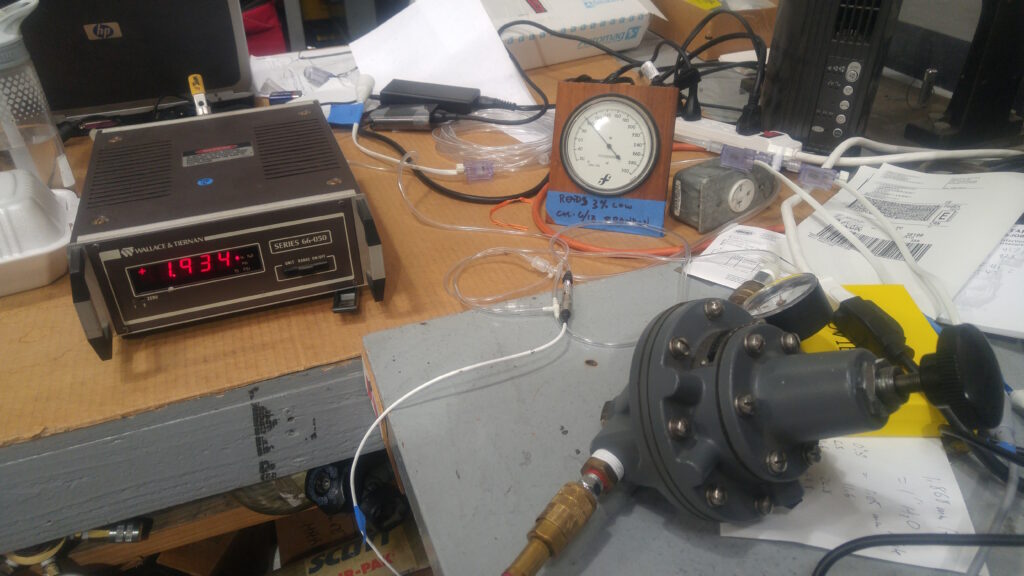 Wallace & Tiernan precision pressure gauge beside a dial reference gauge with a note flagging it as reading 3% low