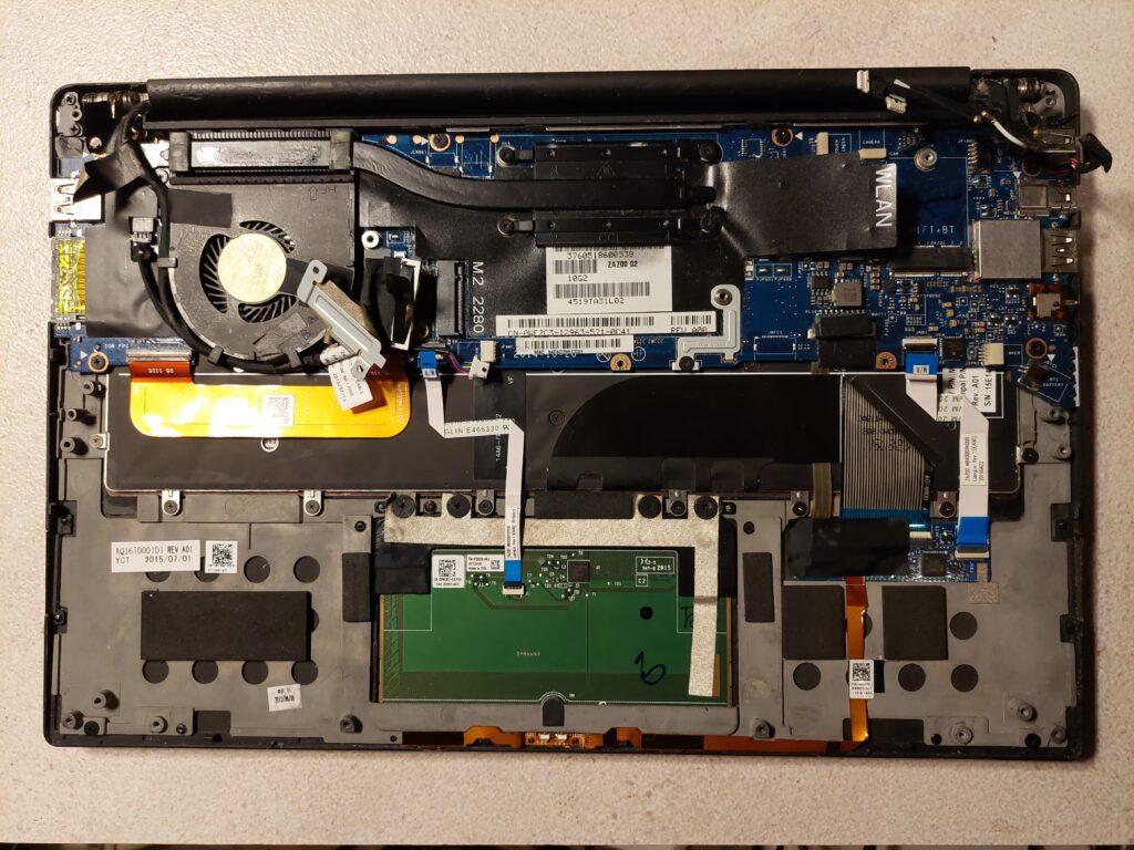 A laptop teardown in progress on a work table: components, screws, and tools laid out in order