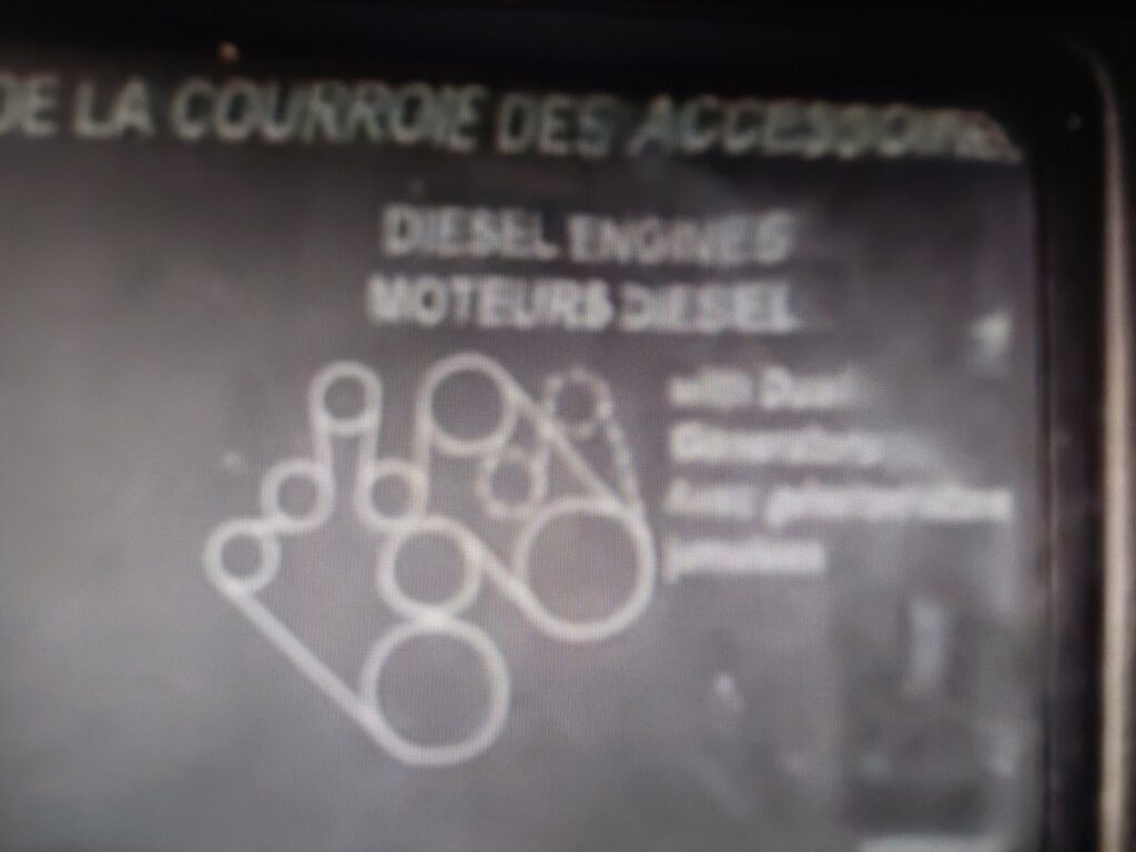 The accessory drive belt routing diagram on a decal under the hood, photographed before the front of the engine was disassembled