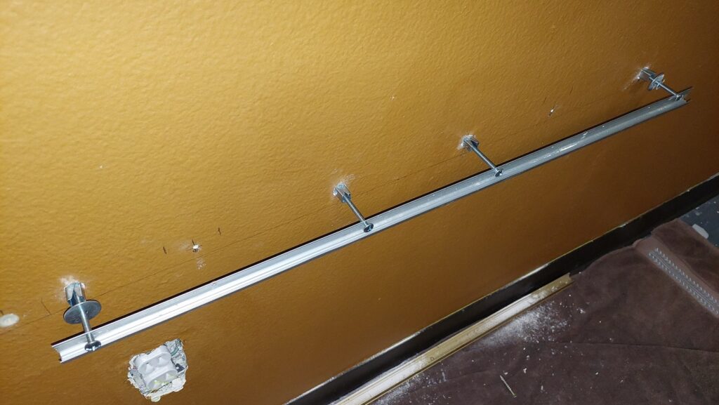 A metal mirror-mount channel screwed to the wall in a level horizontal run, with a row of wall anchors set along it and a mirror clip at one end