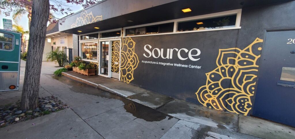 The finished mural across the front elevation of a single-story building: a large gold mandala on dark gray stucco beside the business wordmark