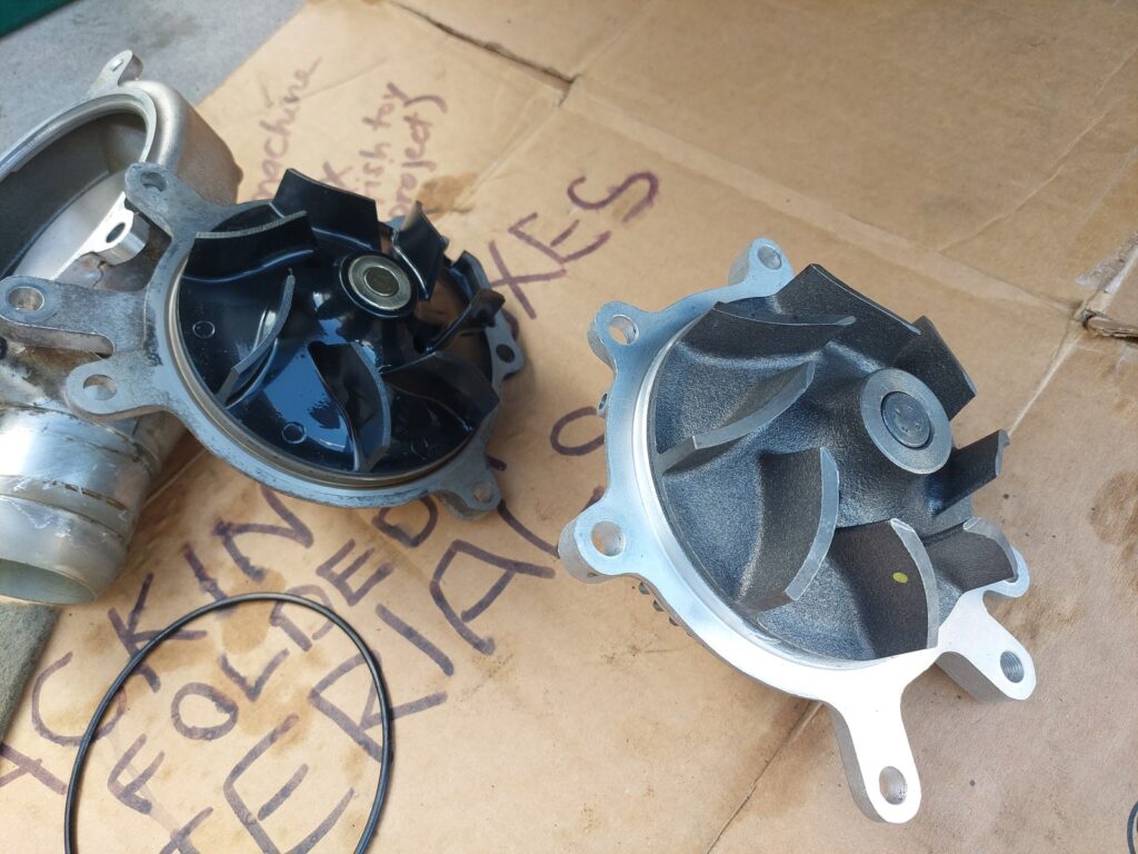 The old and new water pumps set side by side on labeled cardboard, impellers visible