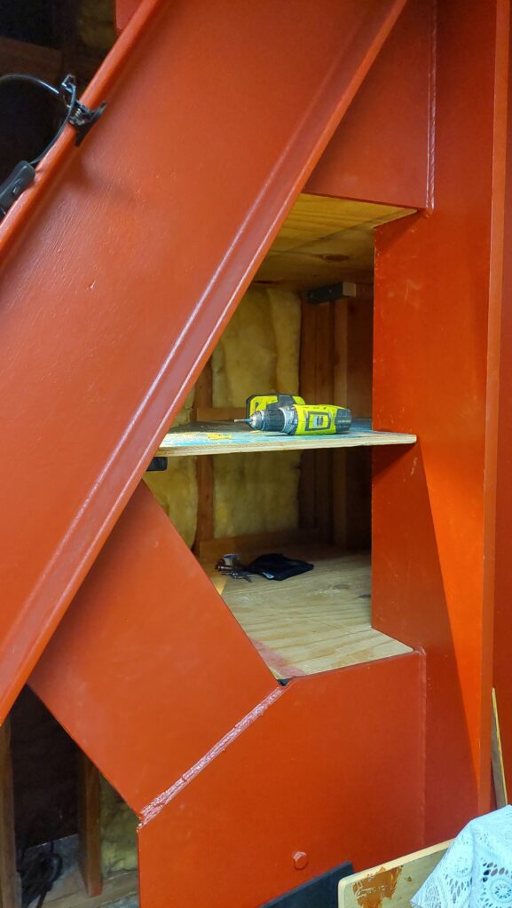 The finished shelves seated in the nook, each one cut to a different angle where the orange diagonal steel brace passes through the space