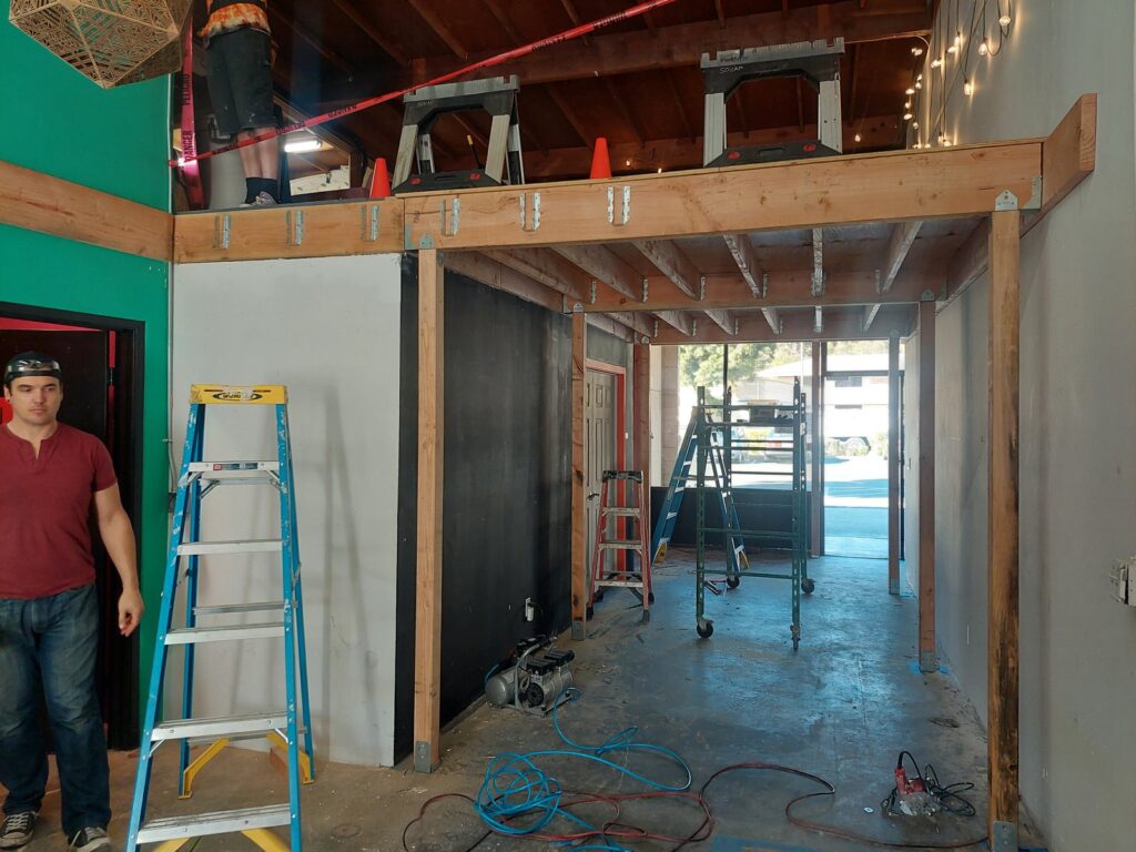 New floor joists spanning what had been a two-story open void at CoLab, seen from below with a volunteer and a stepladder alongside