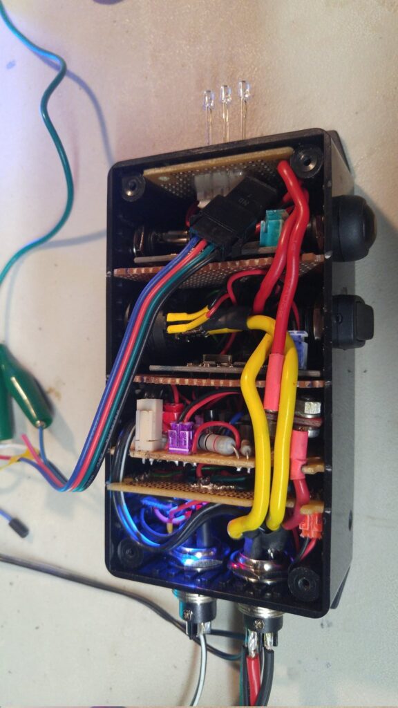The control box with its lid off, showing hand-built circuit boards stacked in tiers with color-coded wiring and panel-mount connectors at the base