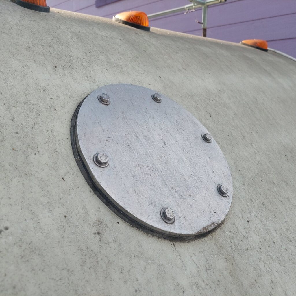 The mount cap bolted flat to the RV roof with a gasket beneath it, weathered and dirty, clearance lights along the roof edge