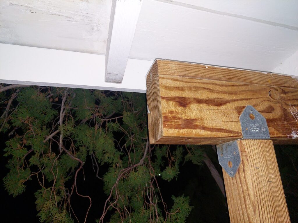 A 4x6 beam meeting a 4x4 post at the porch doorway, joined with galvanised structural brackets, seen from below against the white soffit