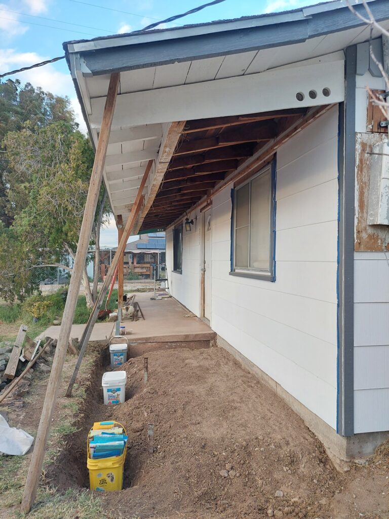 The same porch section cleared and excavated, the roof still carried on diagonal props, soffit removed to expose the rafters above