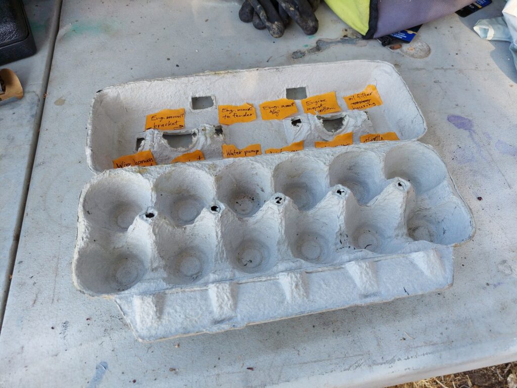 A cardboard egg carton used as a parts organizer, its labeled compartments empty at the end of the job