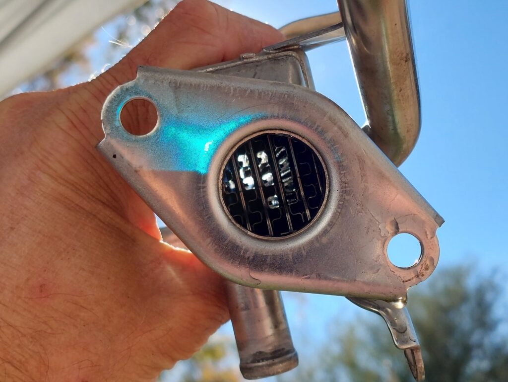 The EGR heat exchanger held up against the sky after cleaning, daylight visible through the individual passages of its core