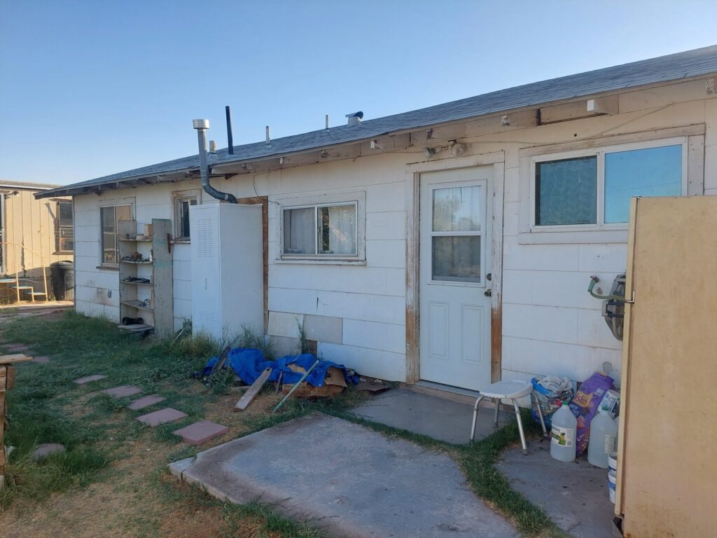 The back of the house with failing paint, weathered siding and stored items across the yard