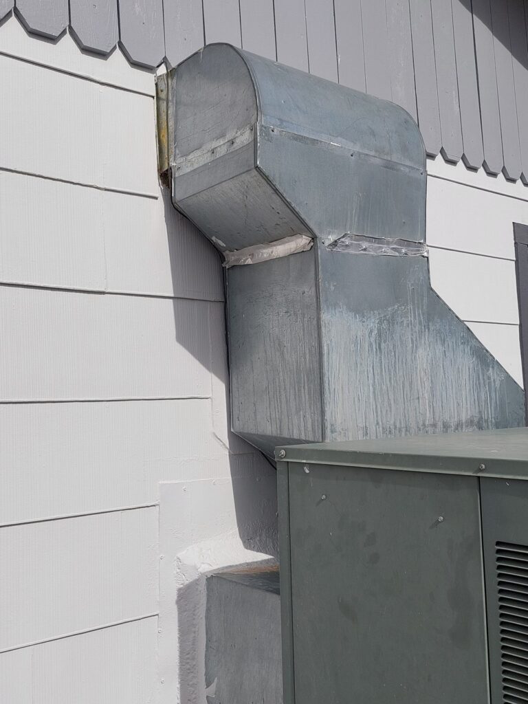 The same duct with new siding around it and sheet-metal flashing formed to the duct’s angles