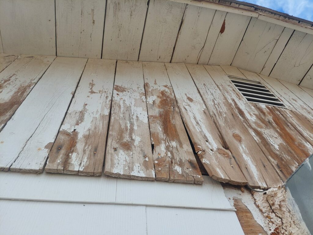 Gable boards split, cupped and shedding paint, with bare weathered wood showing through
