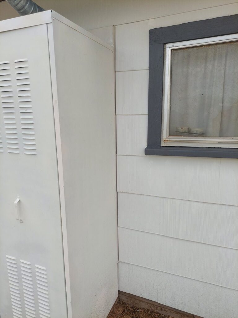 The same wall finished, with new siding running behind the water-heater housing and trim around the window