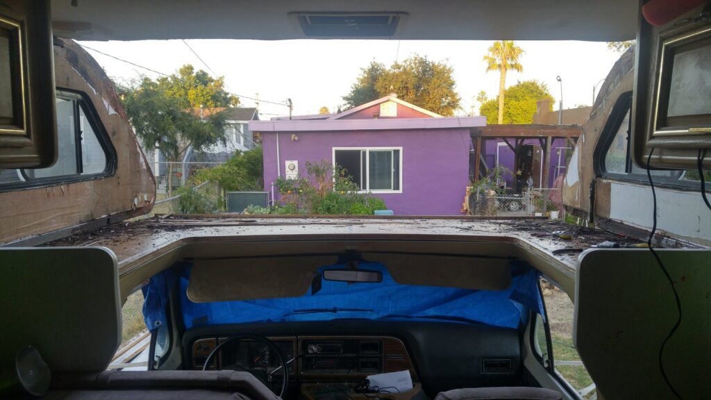 The cabover stripped out entirely, seen from inside the coach: daylight and a neighboring house visible straight through the opening where the bunk structure used to be