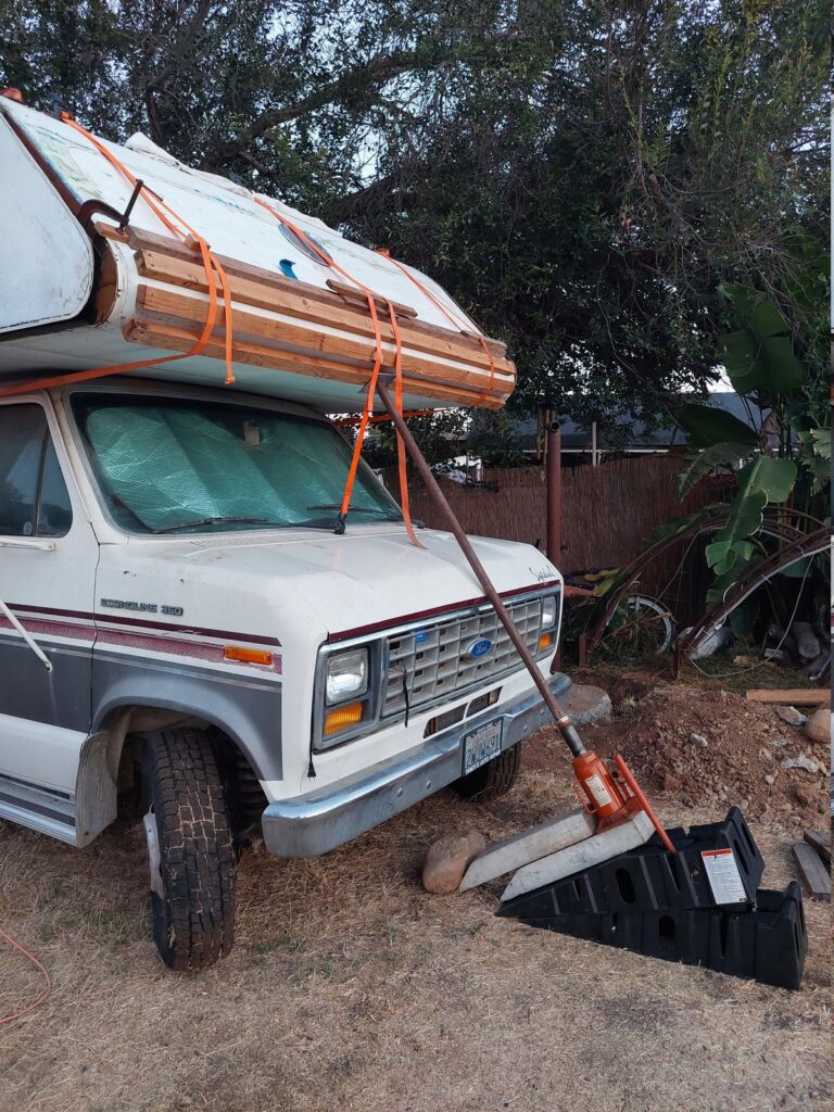 The exterior fiberglass held against the frame by ratchet straps, with a bottle jack on car ramps and stacked blocks providing upward pressure