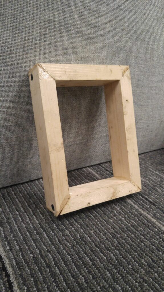 A shallow rectangular box mitered from one-by-two lumber, standing on carpet
