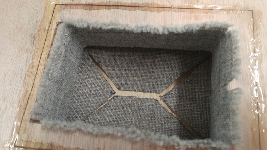 The recess of a pass-through box seen from the front, lined with the acoustic panel’s own grey fabric folded back into it so no bare wood is visible
